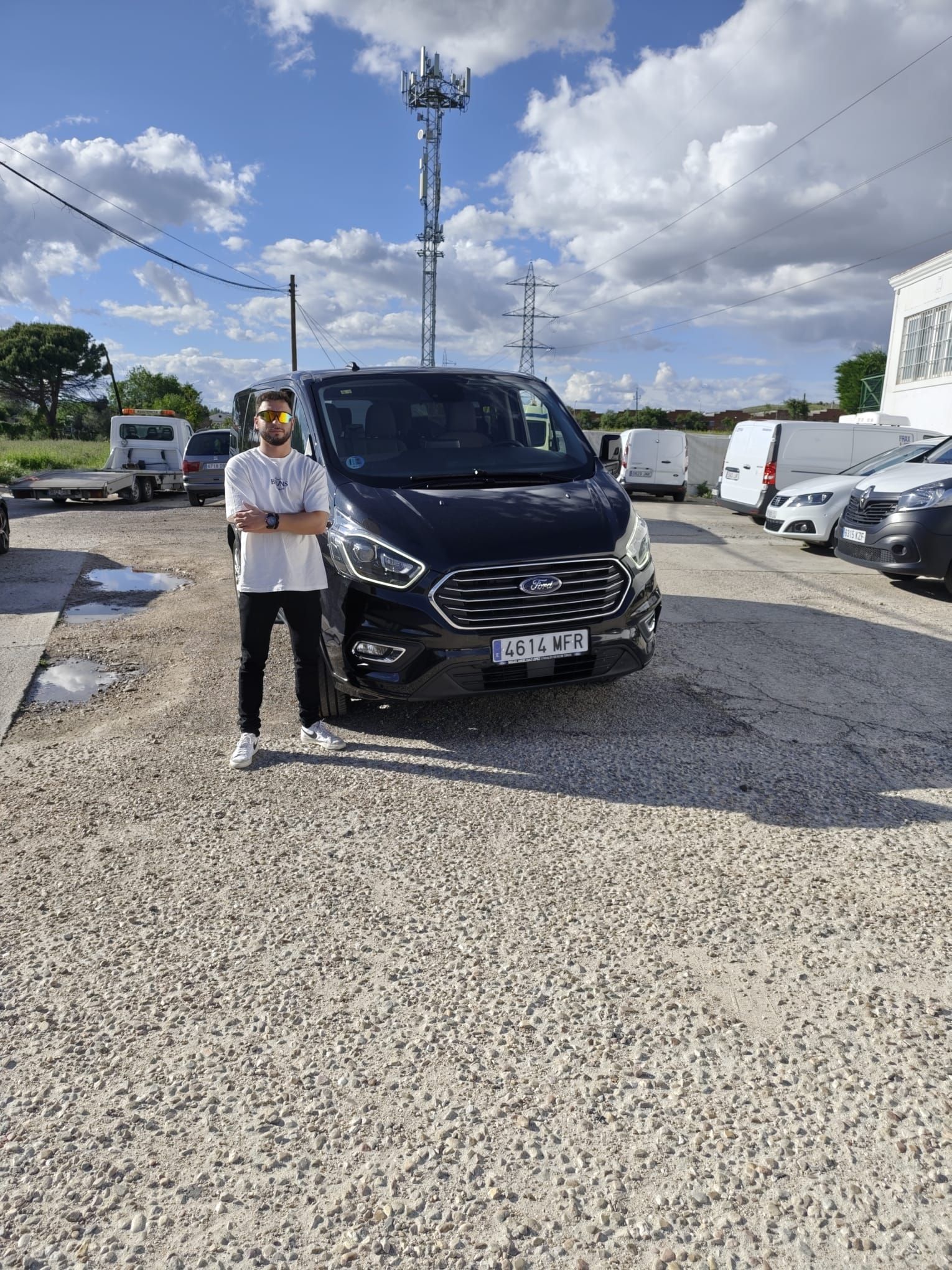 Persona de pie junto a un SUV negro en un estacionamiento de grava bajo un cielo nublado.