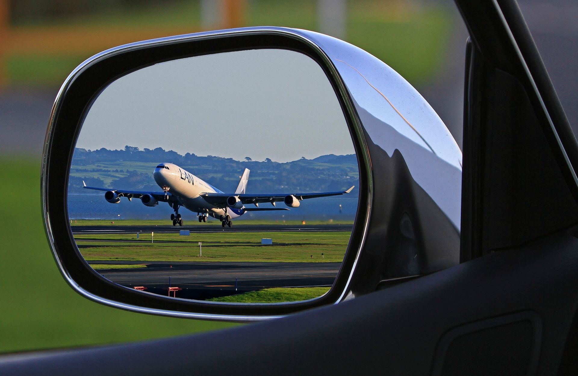 Avión despegando, visto en el espejo retrovisor de un coche.