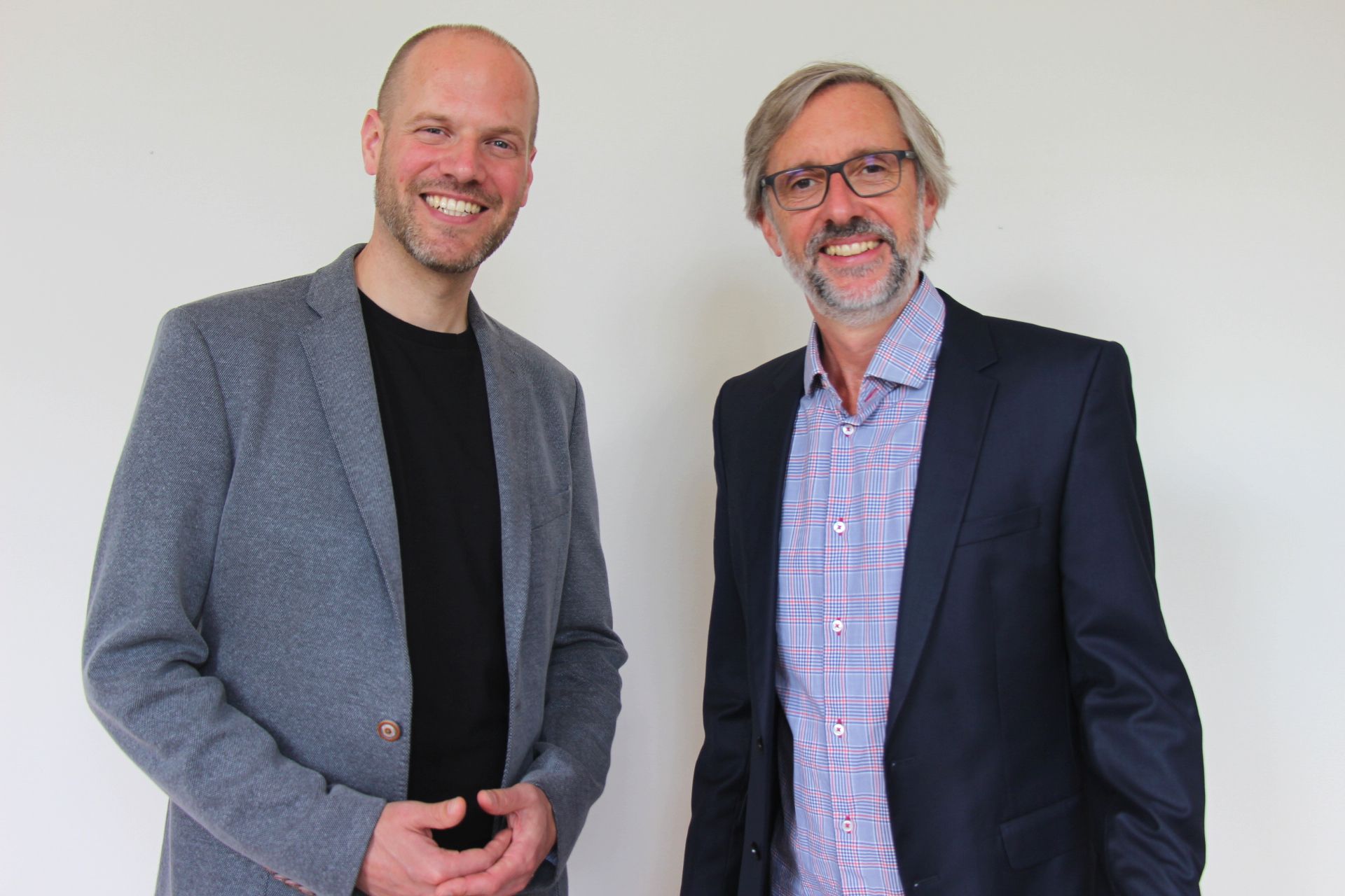 Eine Gruppe von Menschen sitzt an einem Tisch und schaut auf ihre Laptops. Verschiedene Ausdrucksformen, Sonnenlicht, modernes Ambiente.