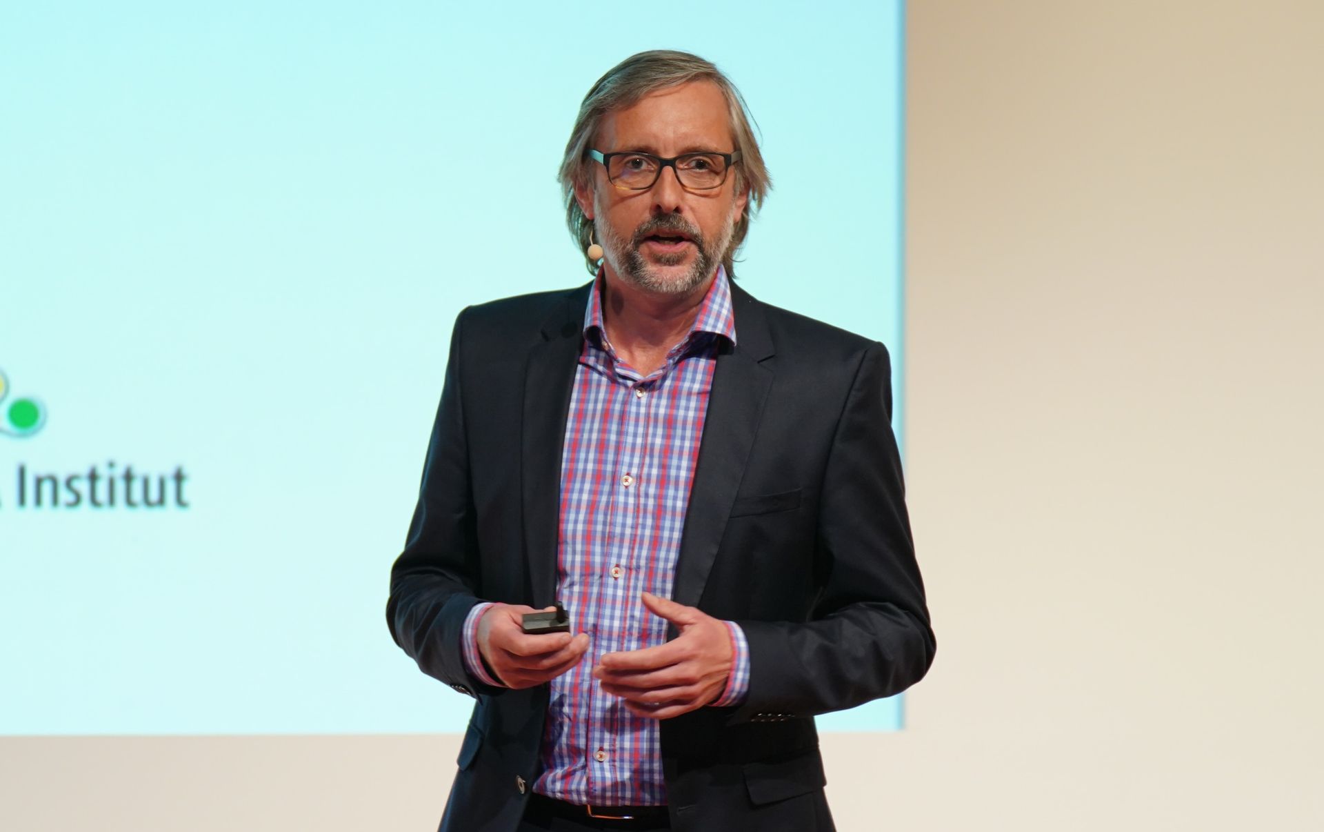 Mann im Blazer spricht bei einer Präsentation; heller Hintergrund.