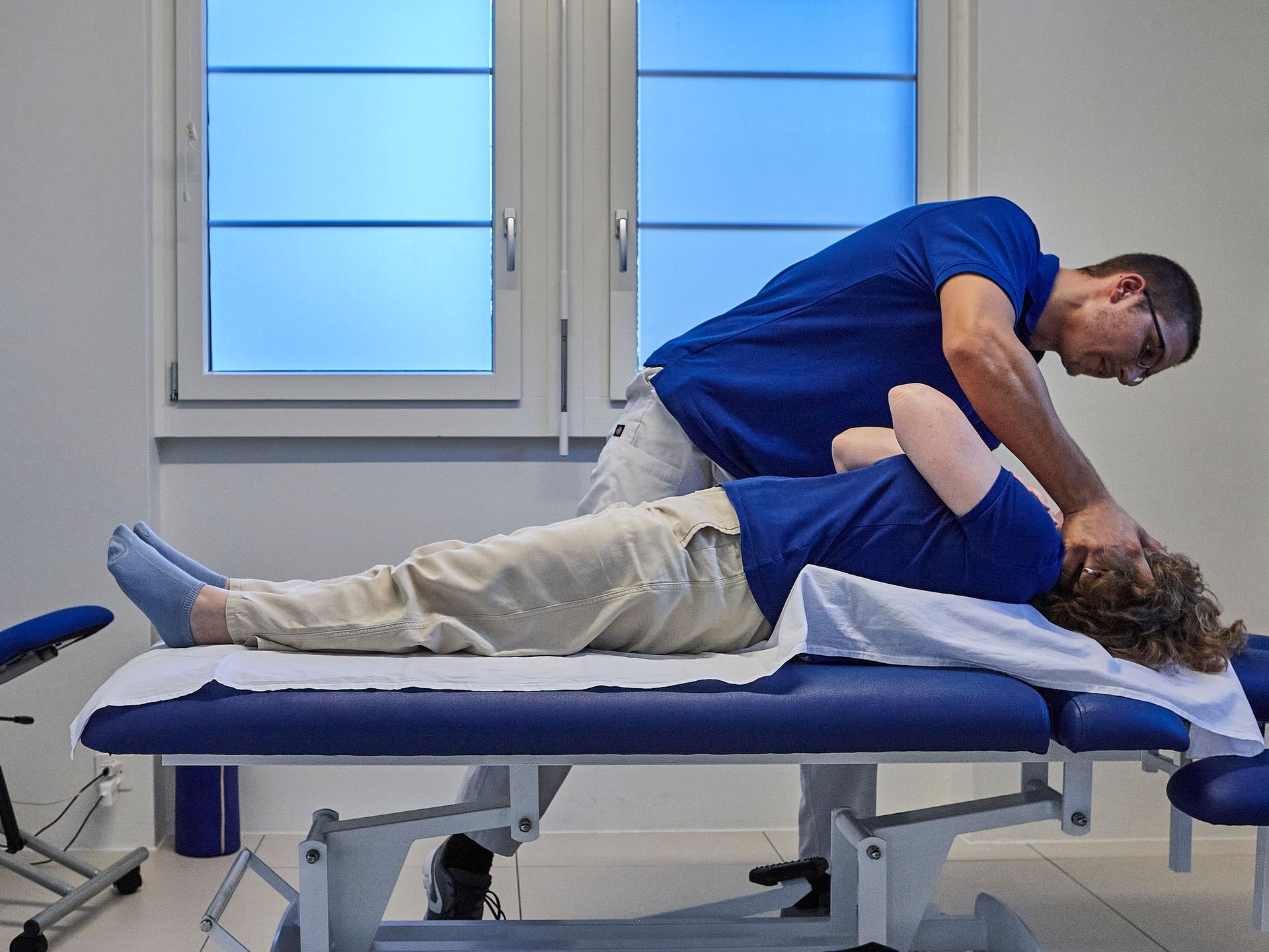Ein Arzt in einem blauen Poloshirt untersucht den Fuss eines Patienten auf einer Untersuchungsliege.