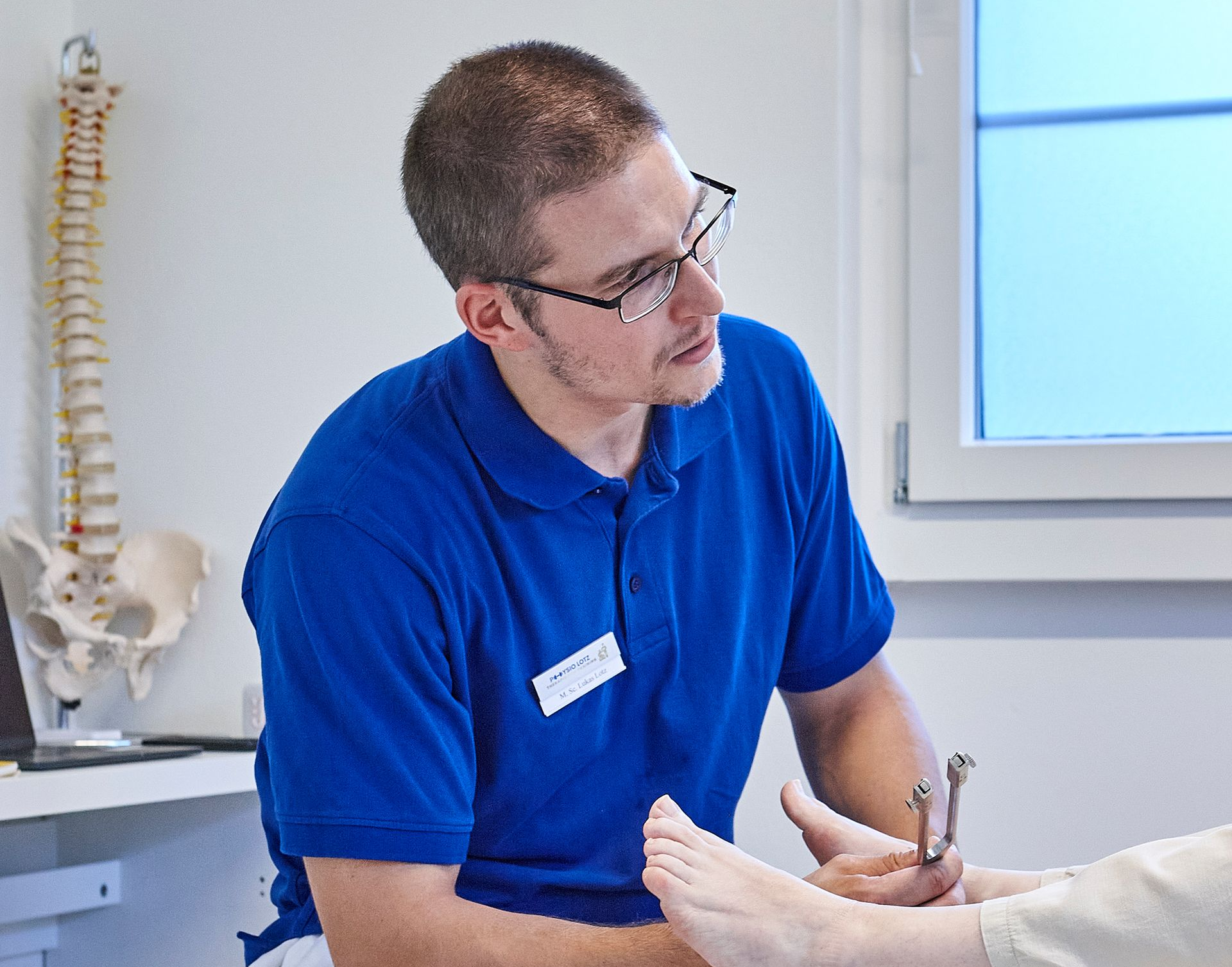 Ein Physiotherapeut in einem blauen Hemd hilft einem Patienten in einem roten Pullover, der sitzt und einen Arm nach oben streckt.