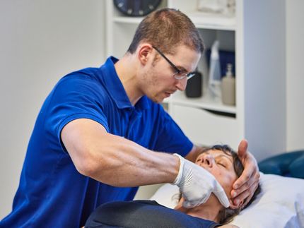 Ein Physiotherapeut massiert die Fusssohle einer Person, die auf einem blauen Kissen ruht.