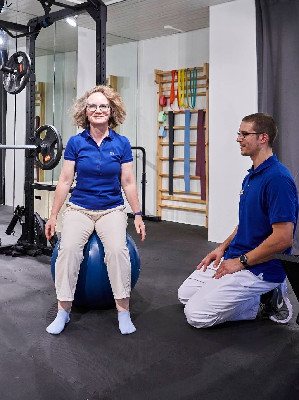 Ein Physiotherapeut beobachtet eine Person, die in einem Fitnessstudio auf einem Gymnastikball sitzt.