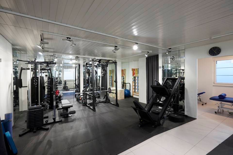 Ein Fitnessstudio voller verschiedener Trainingsgeräte, darunter Hantelständer und eine Beinpresse, auf einem dunklen Gummiboden.