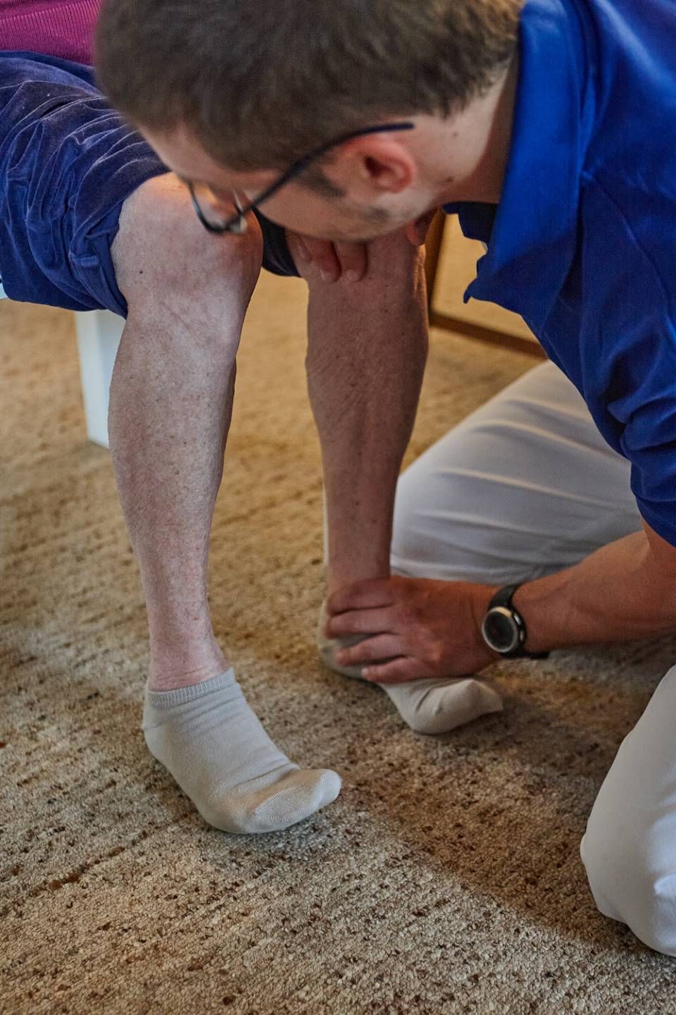 Ein Therapeut in einem blauen Hemd untersucht während einer Physiotherapie-Sitzung den Fuss und den Knöchel eines Patienten.