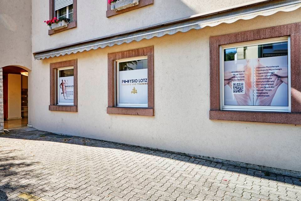 Seitenansicht eines Gebäudes mit drei Fenstern, in denen Informationsplakate und ein QR-Code für ein Geschäft angebracht sind.