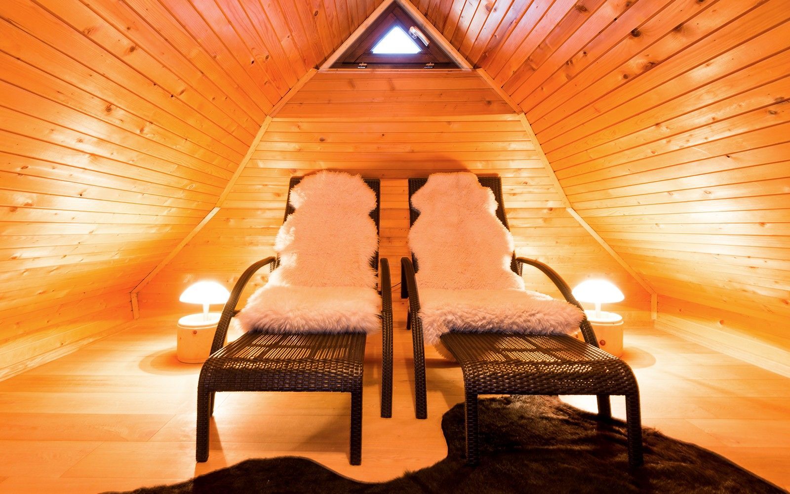 Wellnessbereich, Liegen mit Fell, zwei Lampen rechts und links, helles Holz 