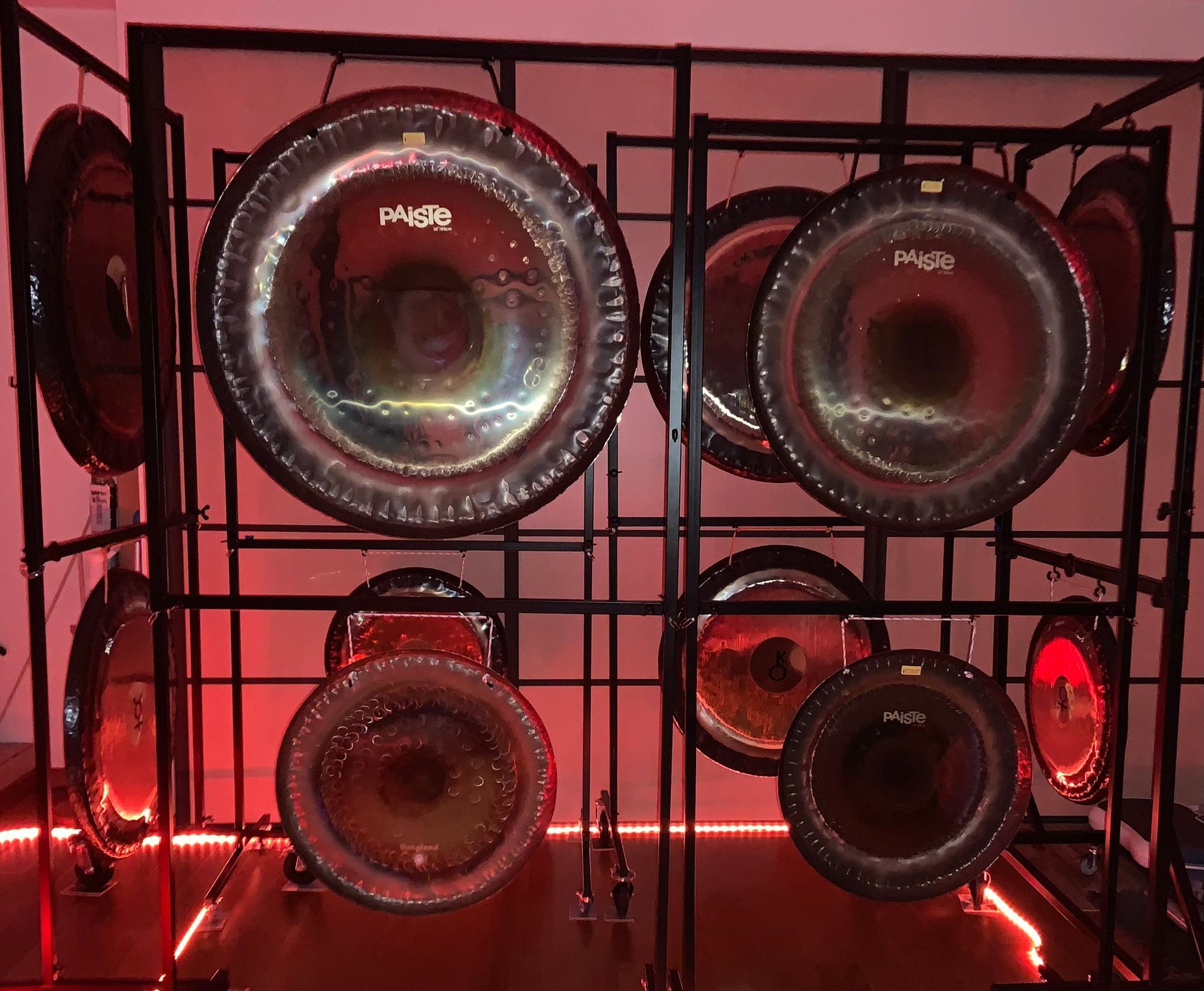 Une collection de gongs sur un support noir, illuminée par des lumières rouges.