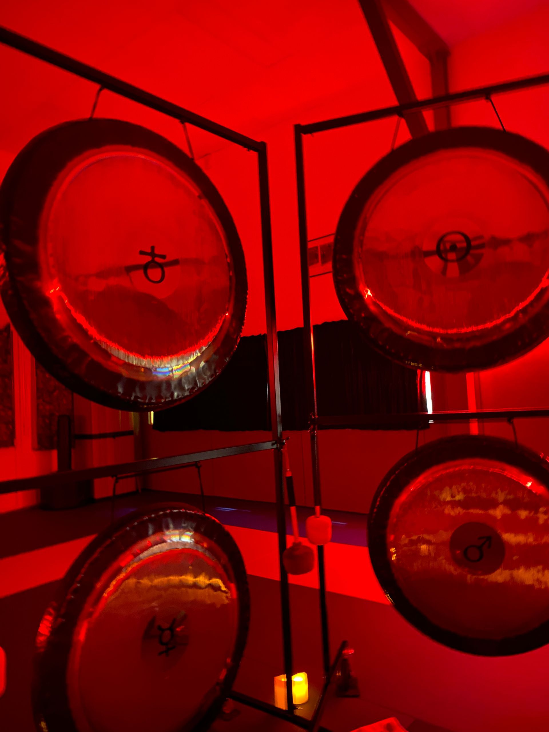 Quatre gongs suspendus dans un cadre, illuminés par une lumière rouge.