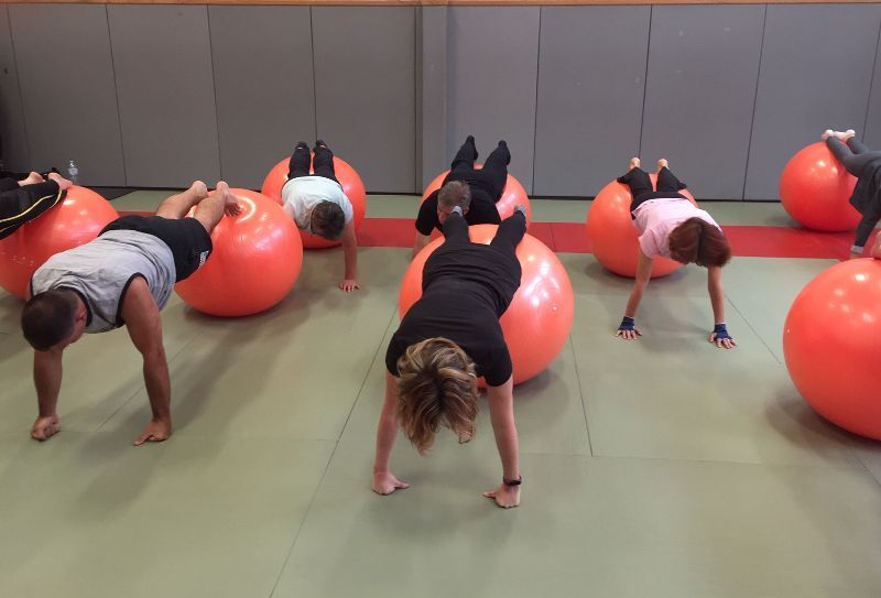 Des personnes font des exercices sur des ballons d'exercice orange, en faisant des planches, dans une salle de sport.
