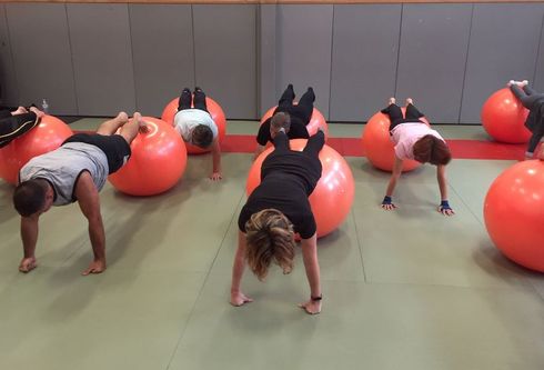 Des personnes font des exercices sur des ballons d'exercice orange, en faisant des planches, dans une salle de sport.