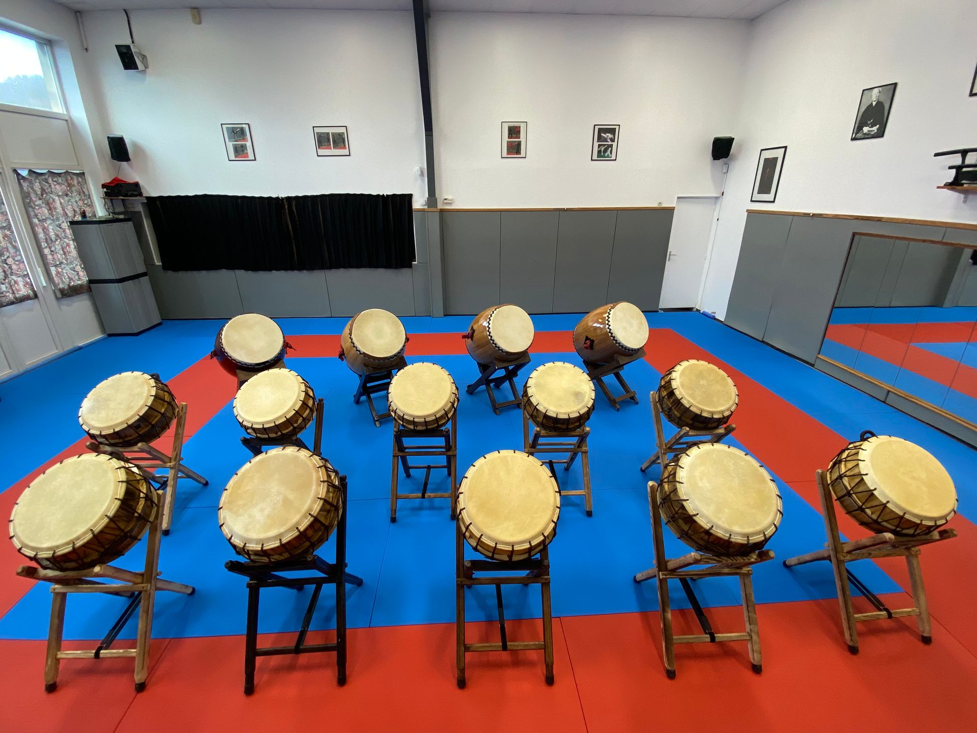 Rangée de tambours taiko sur des tapis bleus et rouges dans une salle de répétition.