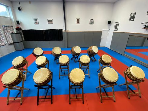 Rangée de tambours taiko sur des tapis bleus et rouges dans une salle de répétition.