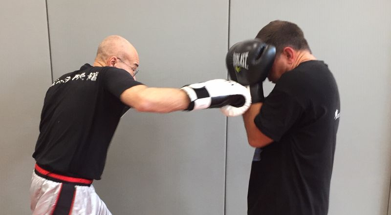 Un boxeur donne un coup de poing à un autre adversaire qui se protège avec des gants. Scène en intérieur.