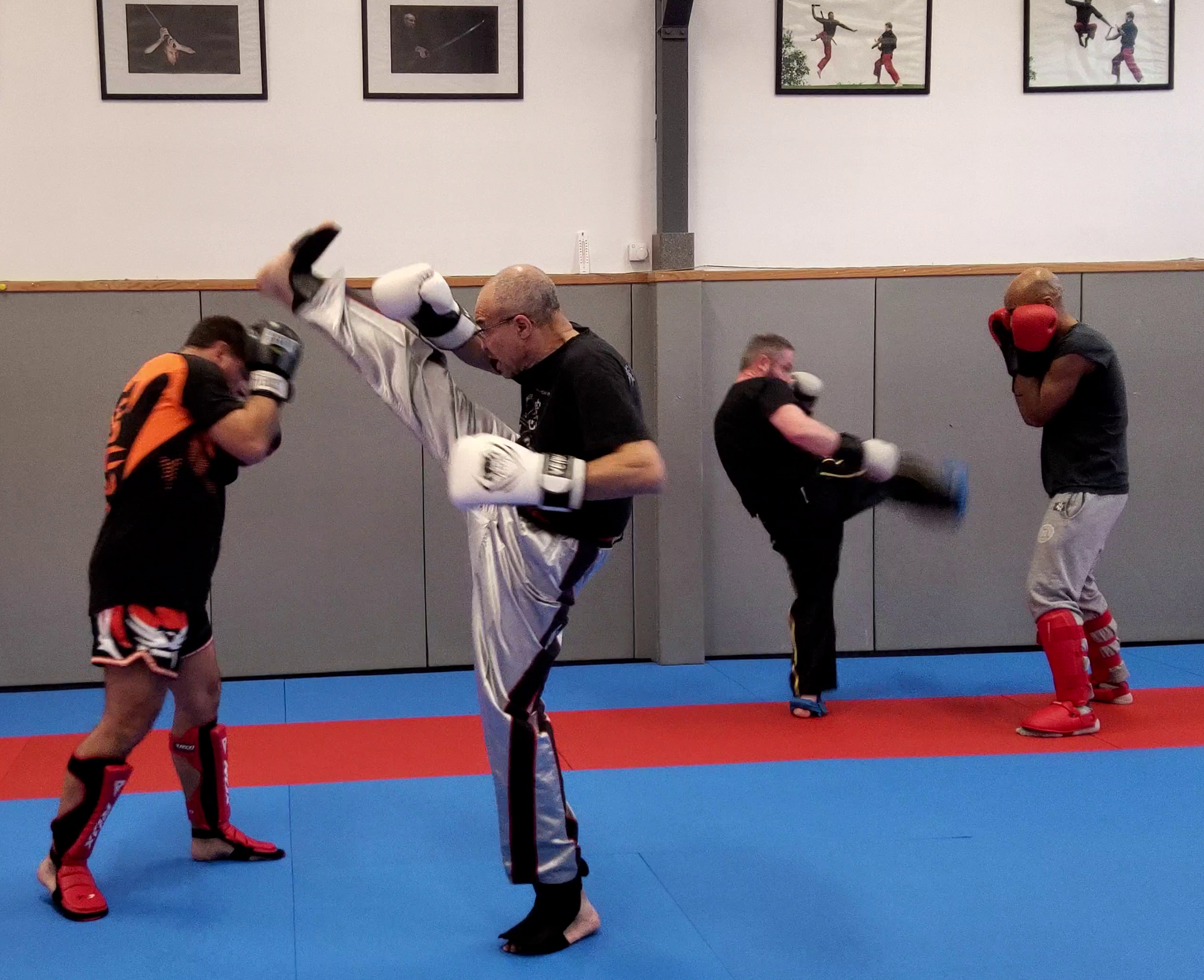 Quatre personnes pratiquent le kickboxing dans une salle de sport. L'une d'elles exécute un coup de pied haut.