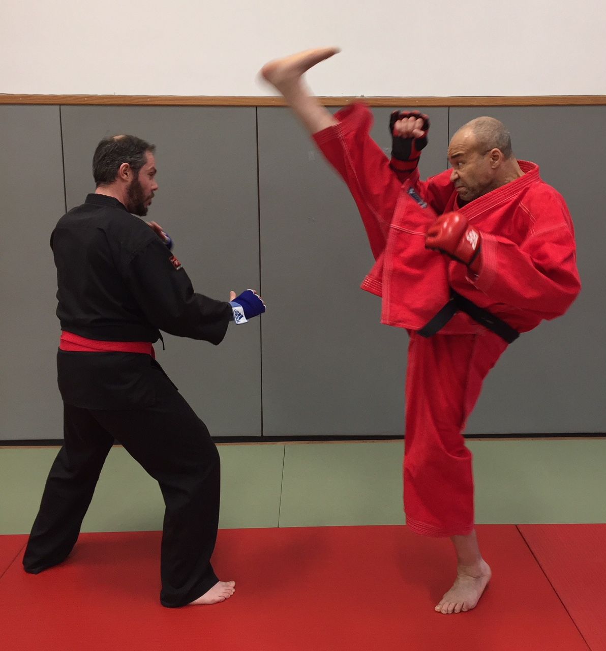 Un pratiquant d'arts martiaux en kimono blanc exécute un coup de pied haut vers un partenaire d'entraînement.