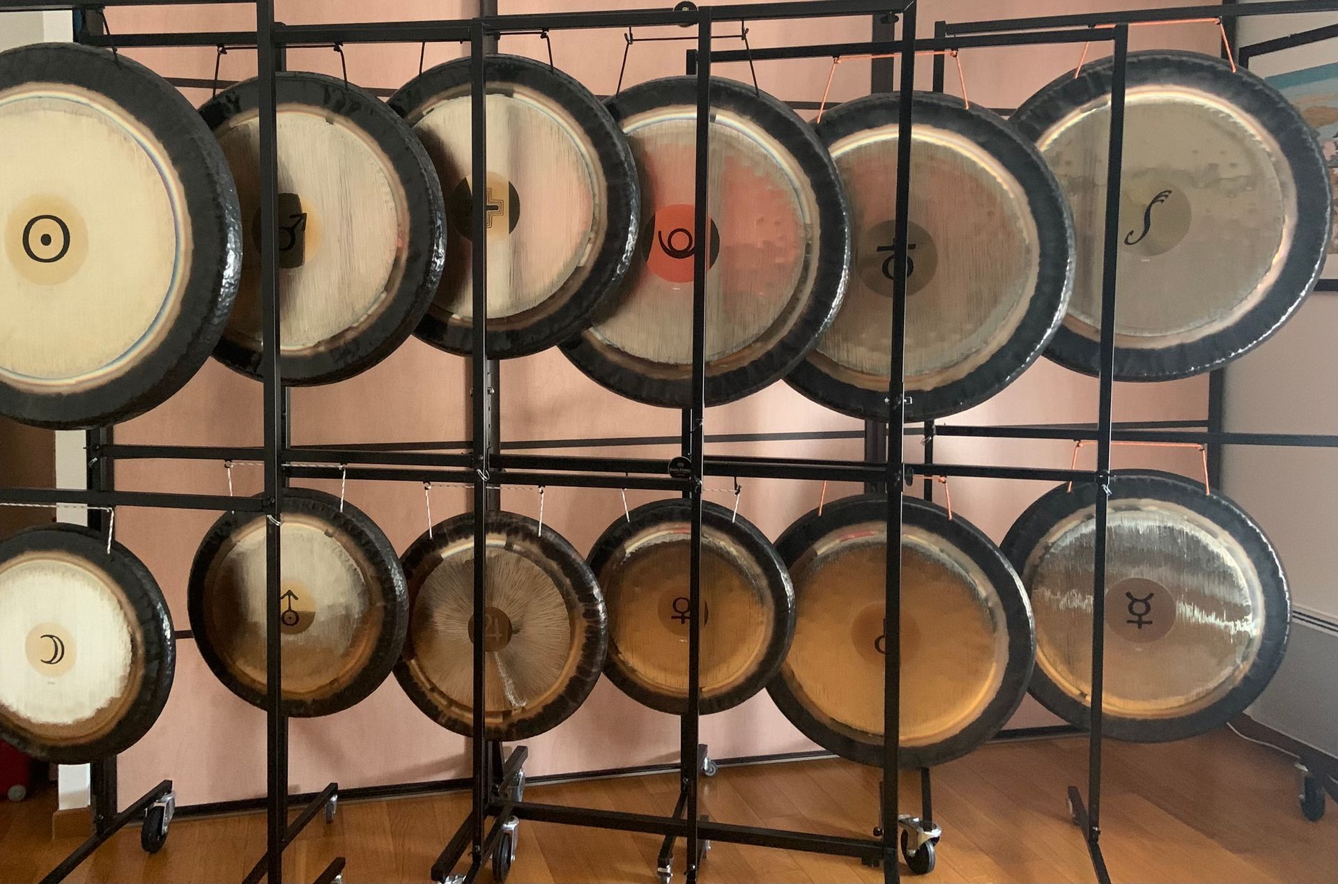 Des gongs de tailles différentes, suspendus à des supports en métal noir, sont disposés à l'intérieur, contre un mur neutre.