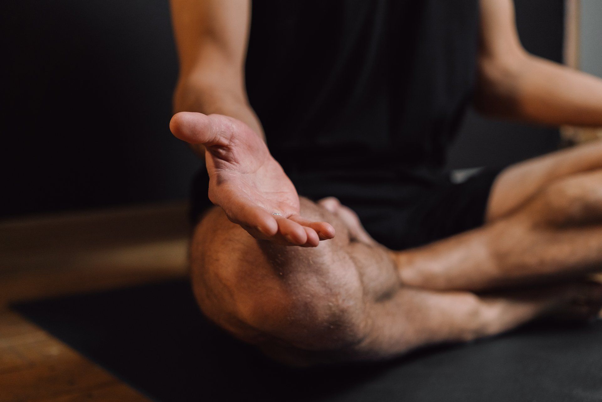 Personne en position du lotus, main gauche ouverte, méditant sur un tapis noir.