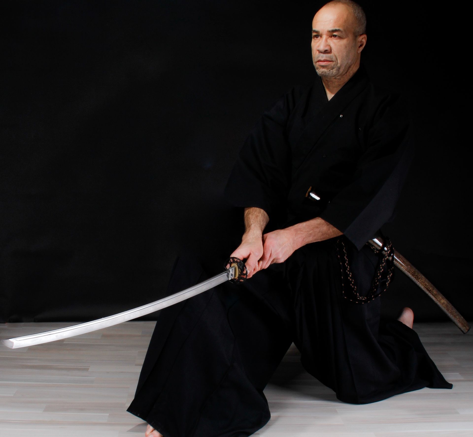 Deux hommes pratiquent le combat à l'épée, l'un vêtu de blanc, l'autre de noir, dans un dojo.