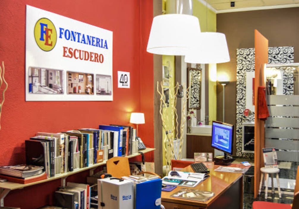 Interior de una tienda de artículos de fontanería con escritorio, estanterías y paredes rojas. Un cartel dice 