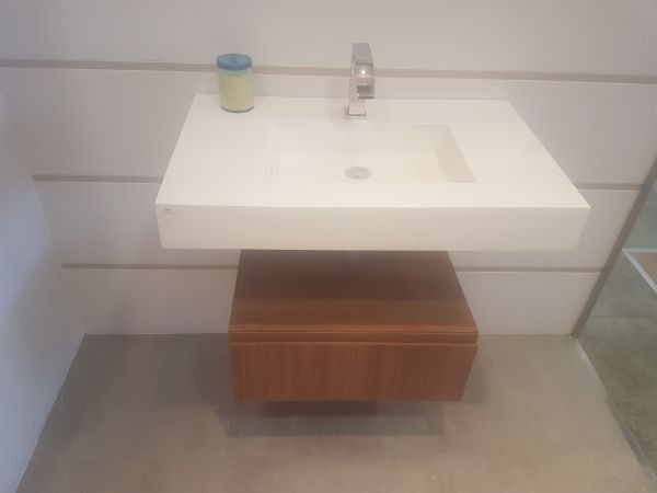 Un lavabo cuadrado blanco de pared con grifo cromado. Debajo hay un mueble de madera.
