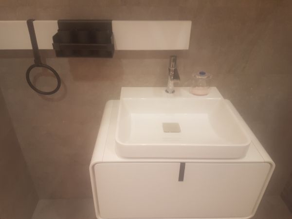 Lavabo blanco sobre un mueble a juego. Encima, un estante con un toallero de aro.