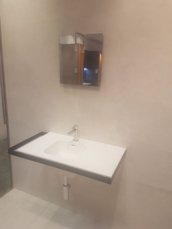 Lavabo blanco con grifería cromada y mueble espejo montado en pared de color claro.