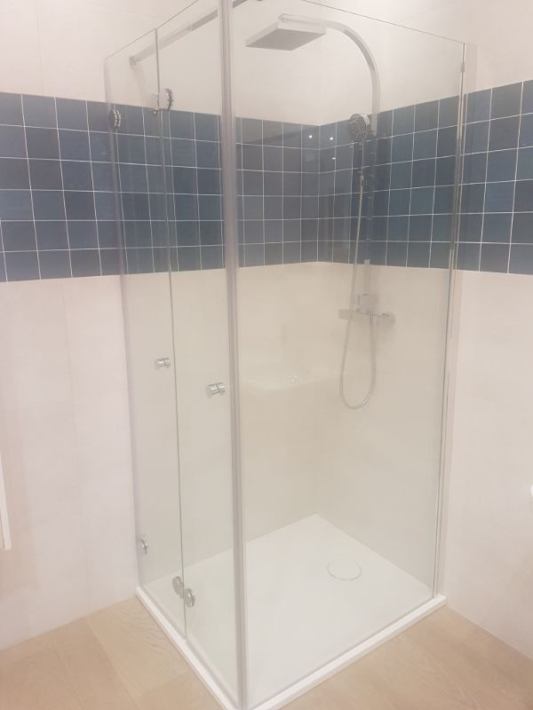 Cabina de ducha de esquina con puertas de vidrio y detalles de azulejos azules.