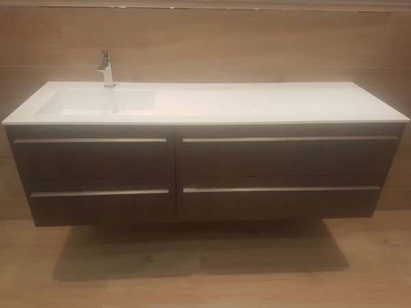 Tocador de baño flotante con cajones color marrón oscuro, encimera blanca y grifería plateada.