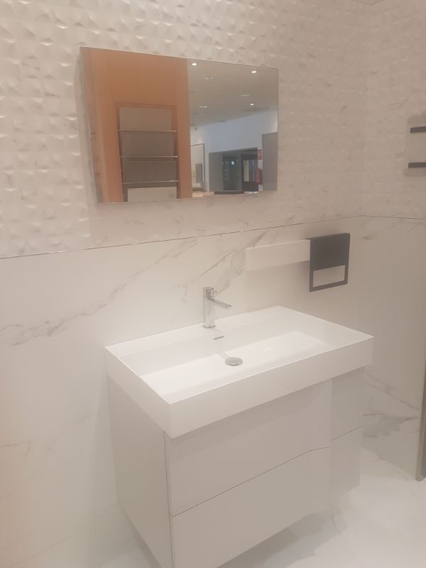 Baño blanco con tocador blanco, espejo cuadrado y pared blanca texturizada.