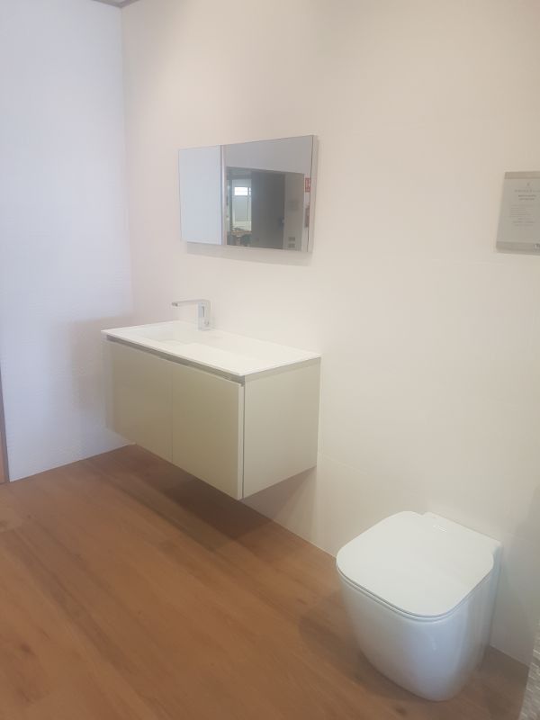 Baño con lavabo blanco de pared, espejo e inodoro. Suelo de madera.