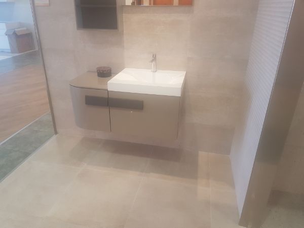 Baño con tocador flotante, lavabo y azulejos de color neutro.