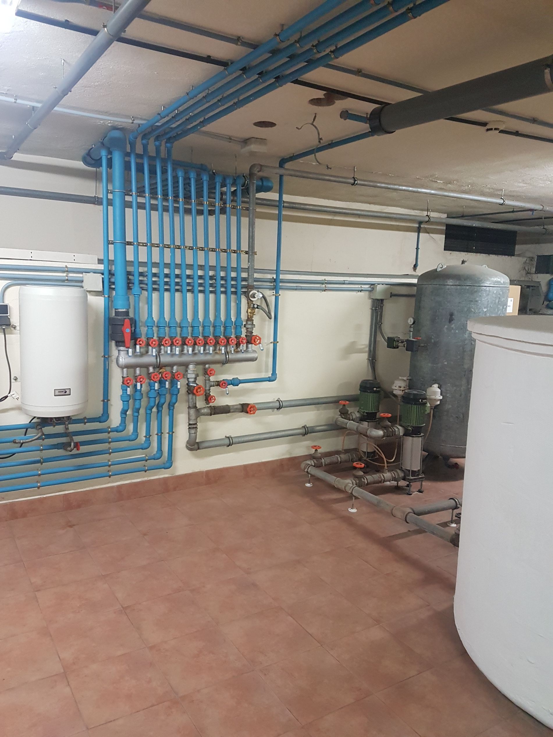 Tuberías y plomería azules en un cuarto de servicio con tanques de agua y equipos de calefacción.