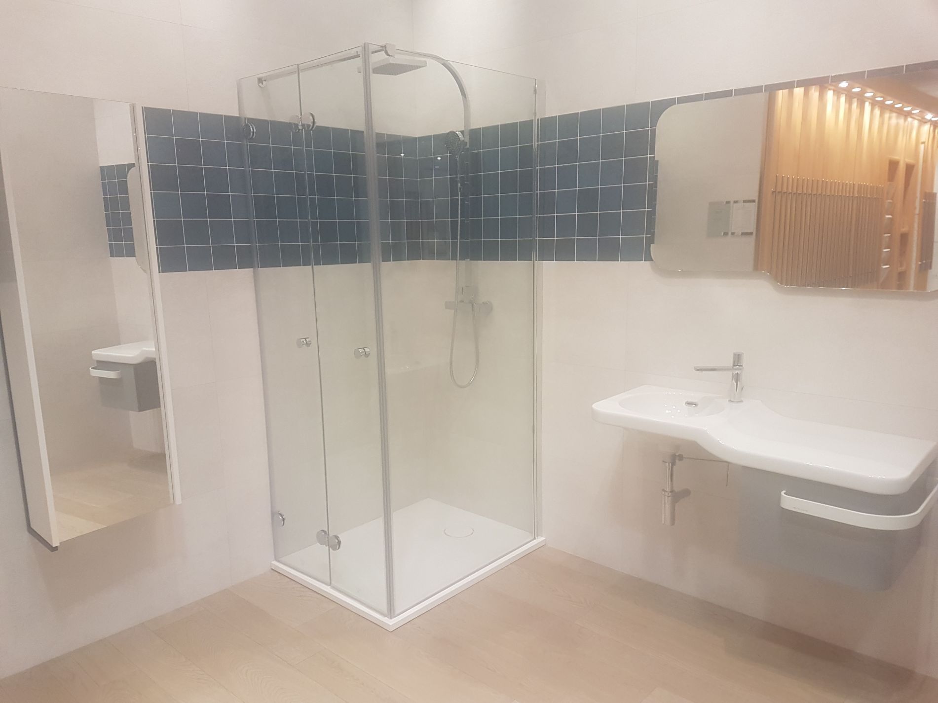 Baño moderno con ducha de vidrio, tocador, espejo y pared con acento de azulejos azul oscuro.