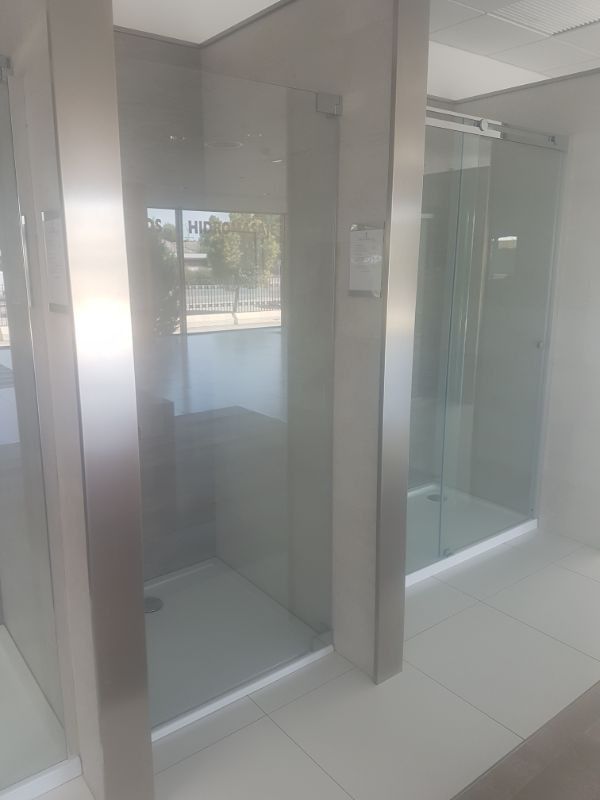 Dos cabinas de ducha de cristal con marcos plateados y suelos blancos en una sala de exposición.