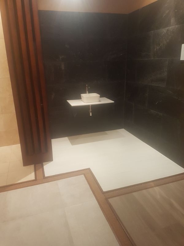 Una ducha moderna con paredes de azulejos negros, piso blanco y un estante con grifo.
