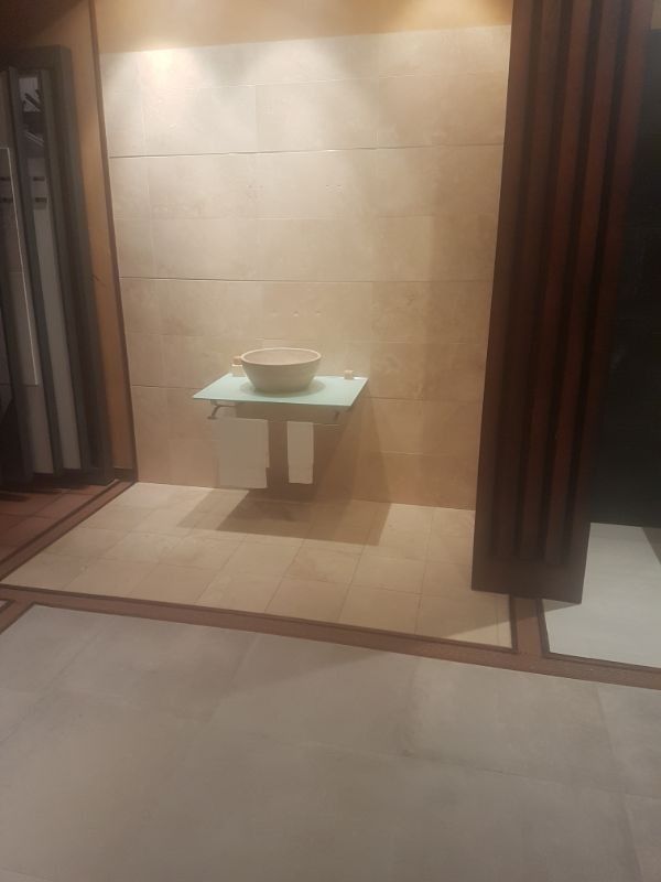 Exhibición de baño con azulejos beige, lavabo flotante y molduras de madera.