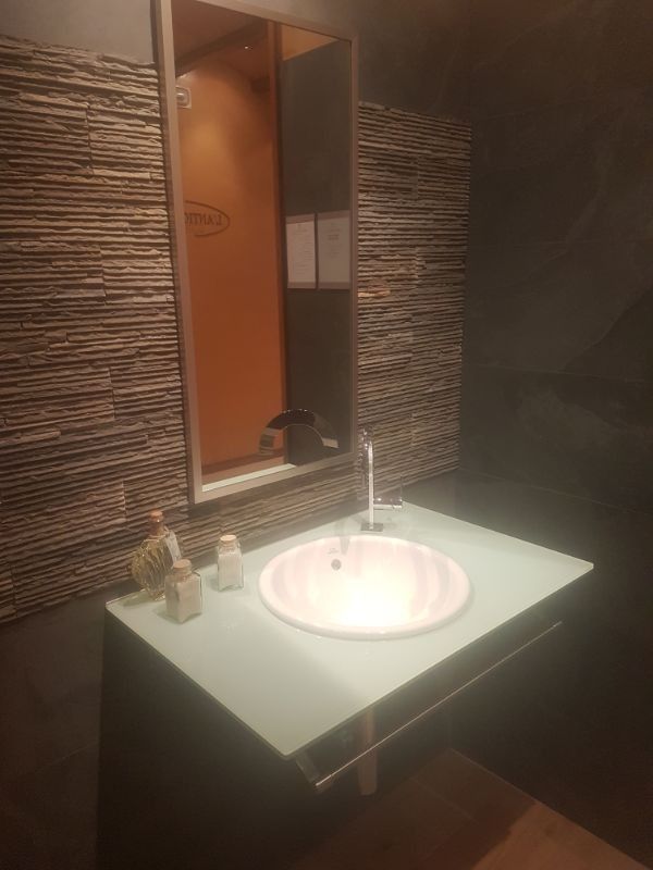 Baño con lavabo blanco, espejo y pared texturizada.