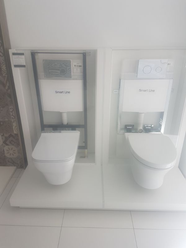 Dos inodoros blancos montados en la pared exhibidos en plataformas en un entorno de sala de exposición.