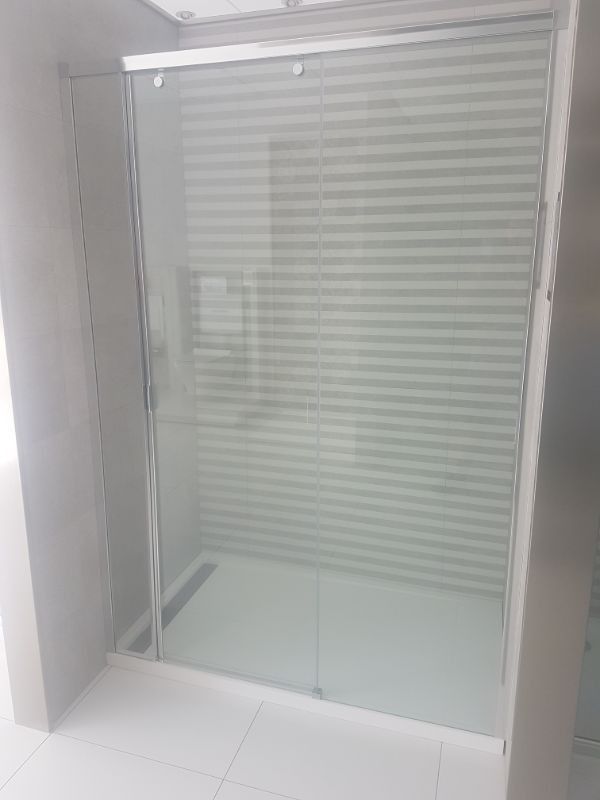Mampara de ducha de cristal con puerta corredera y pared de azulejos rayados.