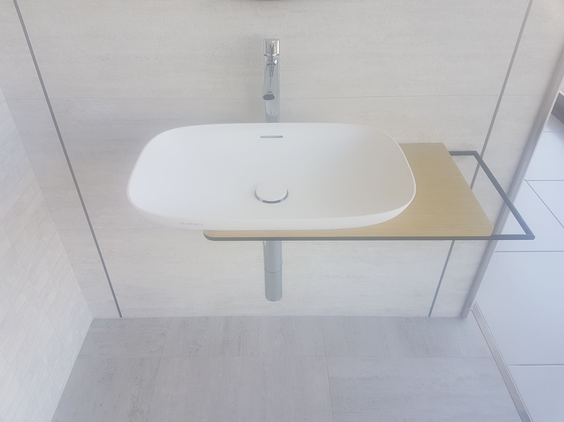 Lavabo blanco con grifo cromado y pequeño estante de madera contra una pared de azulejos claros.
