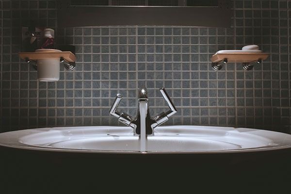 Lavabo de baño con grifería cromada, pequeño fondo de azulejos y portavasos y jaboneras.