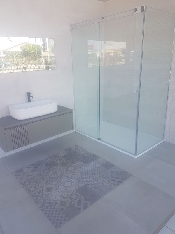 Baño moderno con ducha de cristal, tocador flotante y azulejos decorativos.