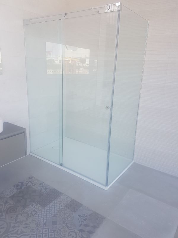 Mampara de ducha de cristal con puerta corredera en baño moderno.