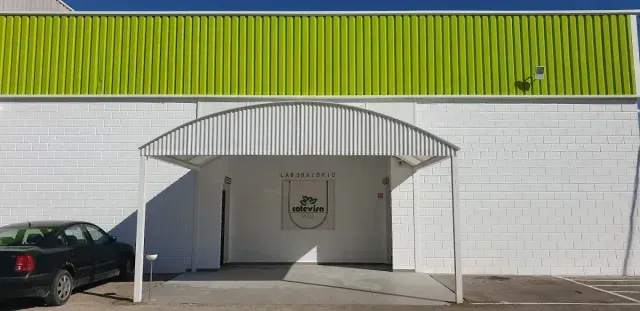Fachada blanca con detalles verdes en el tejado y entrada cubierta, con un coche aparcado a la izquierda.