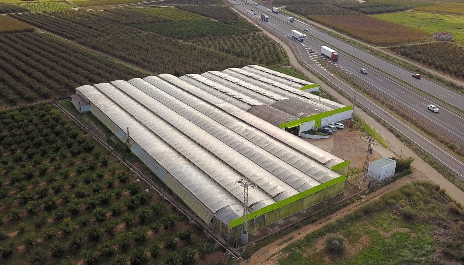 Vista aérea de un complejo de invernaderos junto a tierras de cultivo y una carretera.