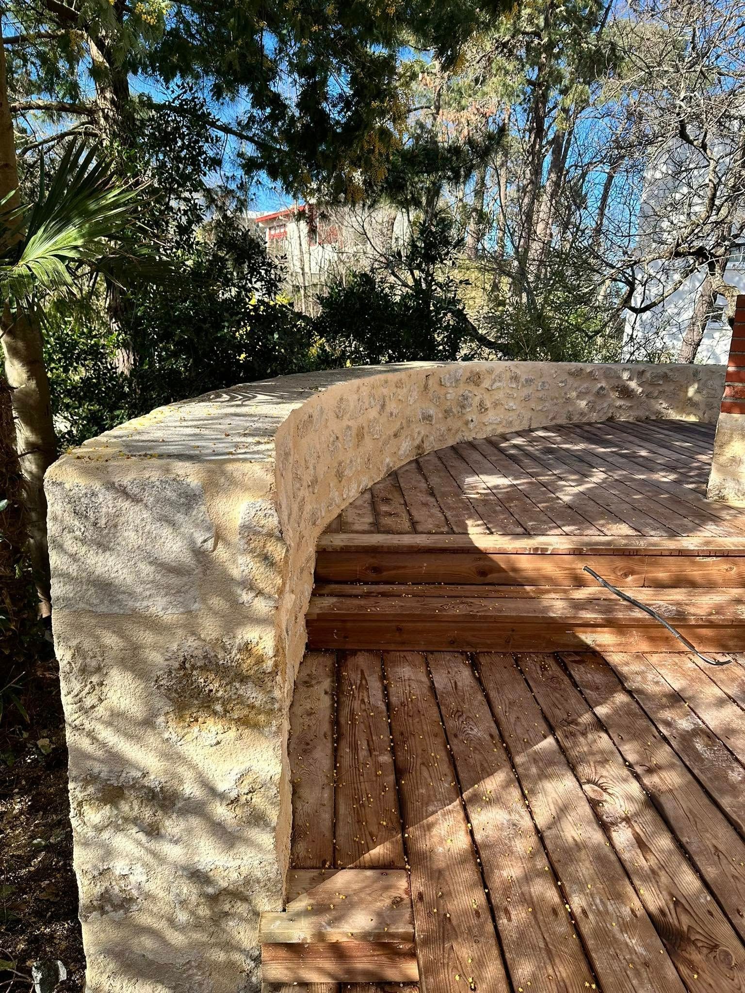 Un mur de soutènement en pierre incurvé borde une terrasse en bois avec des marches