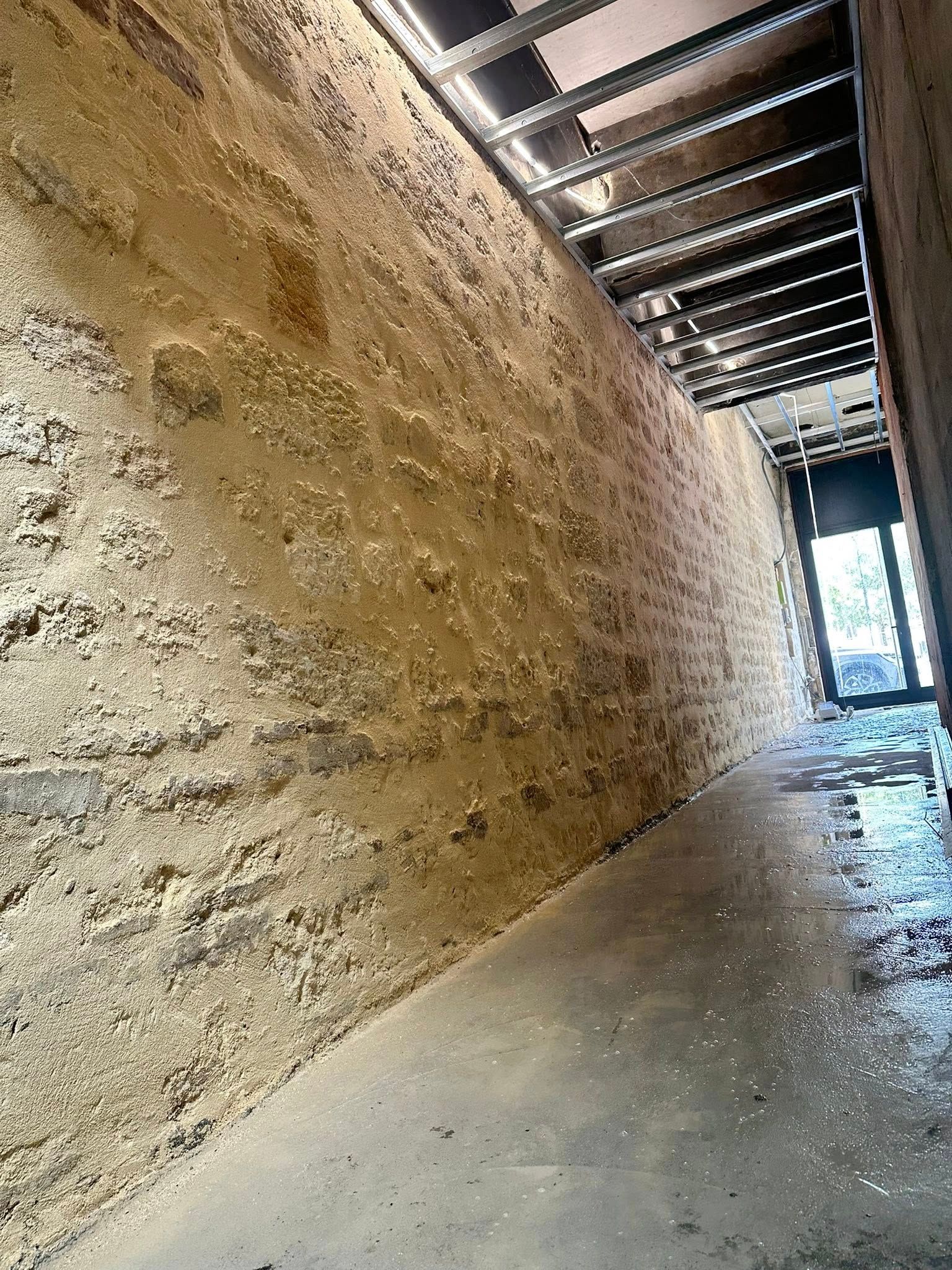 Un mur en pierre, longe un sol en béton en direction d'une porte.