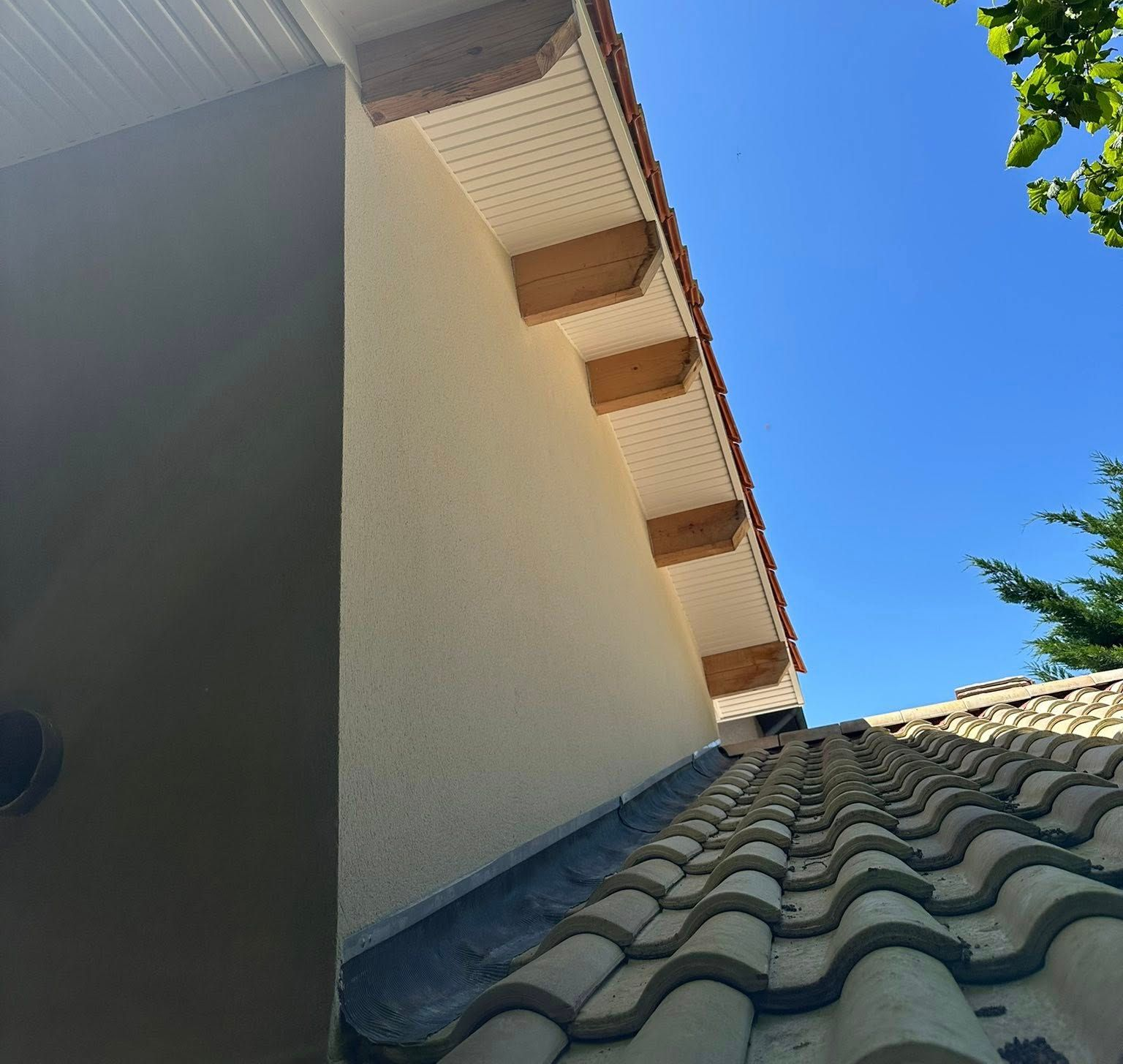 Vue en contre-plongée d'un toit de tuiles rejoignant un mur en stuc clair avec des chevrons de charpente.